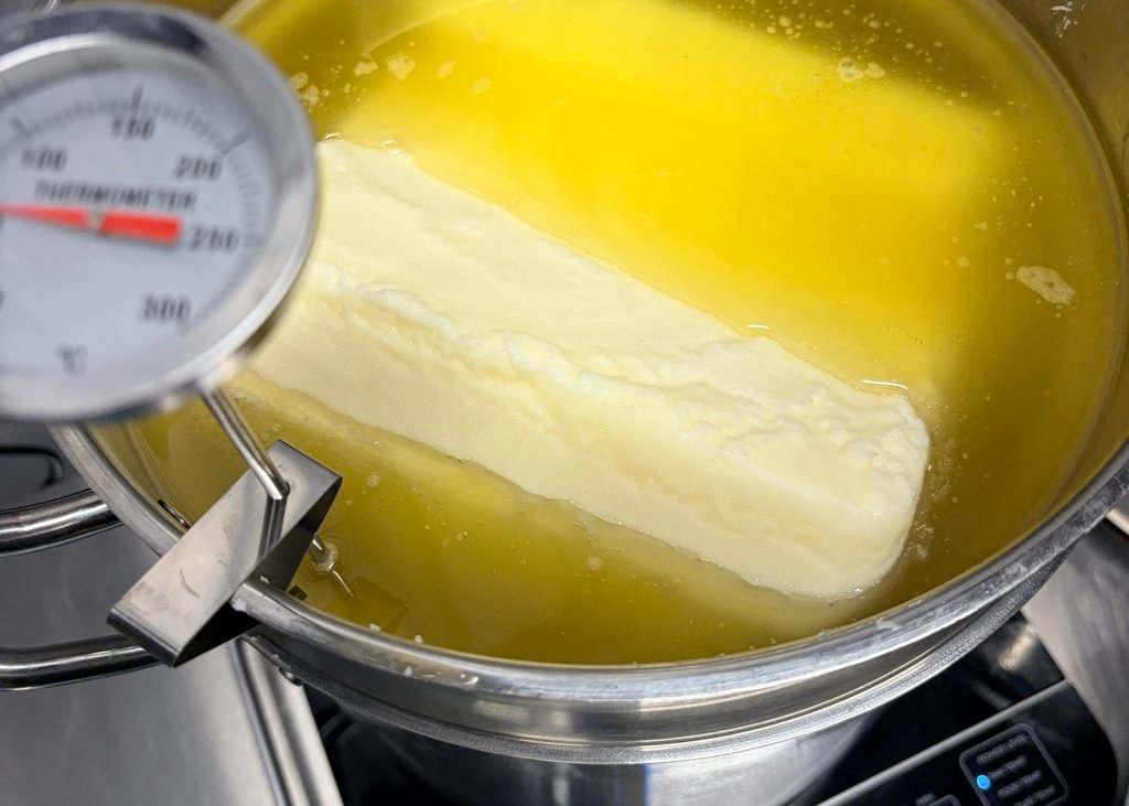 Beef tallow being rendered in a stainless steel pot with a temperature gauge